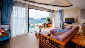A modern living room with a large sliding glass door leading to a pool area, a sofa, a TV, and a dining table. - Kalima Resort & Spa, Phuket (Patong)