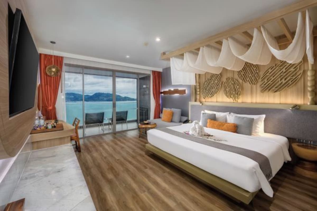 Habitación de hotel con una cama grande, televisión, balcón con vista al mar y piso de madera.