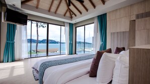 A bedroom with a large bed, a TV mounted on the wall, and a view of the sea through large windows. - Kalima Resort & Spa, Phuket (Patong)