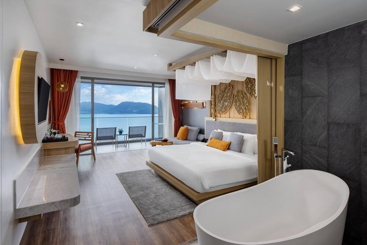 Una habitación de hotel moderna con una cama grande, una bañera, un balcón con vistas al mar y un comedor con una mesa y sillas.