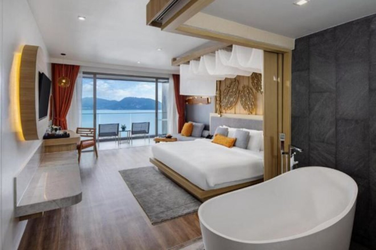Una habitación de hotel moderna con una cama grande, una bañera y vista al mar.