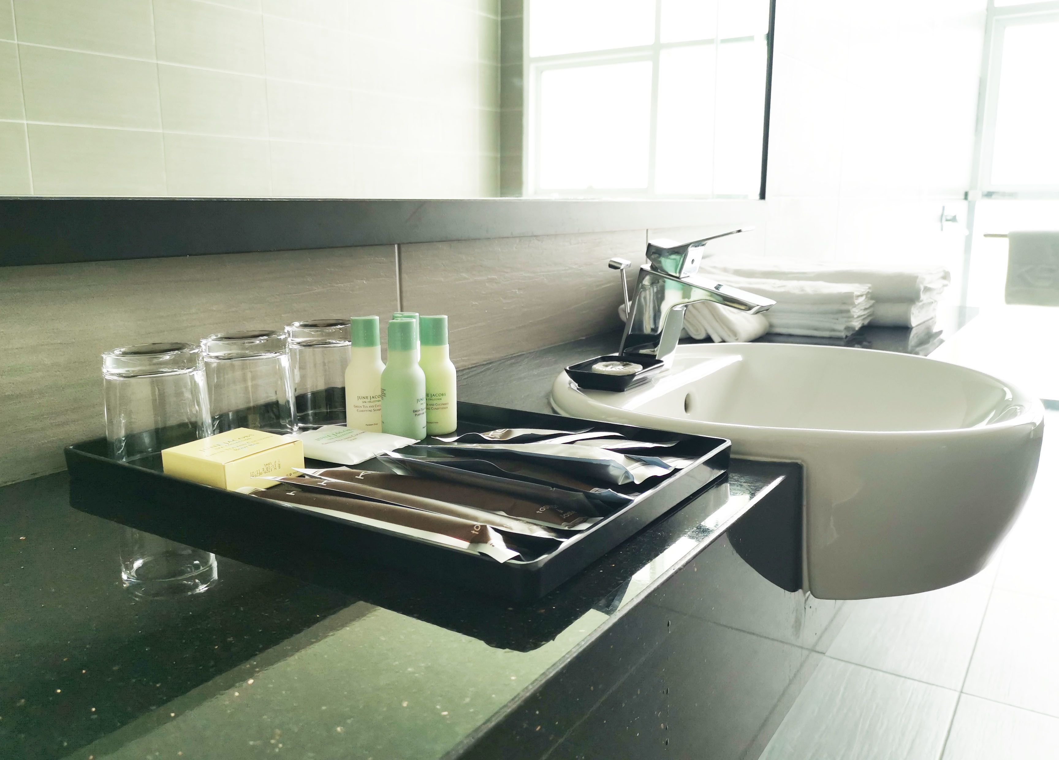 A bathroom with a black tray holding toiletries, a white sink, and a window in the background.