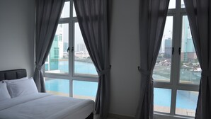 A hotel room with a large bed, a view of a swimming pool, and a cityscape through the windows.