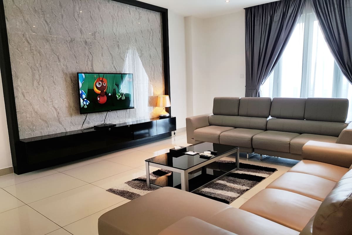 A modern living room with a large flat-screen TV mounted on a marble wall, a grey sofa, a glass coffee table, and a lamp on a side table.