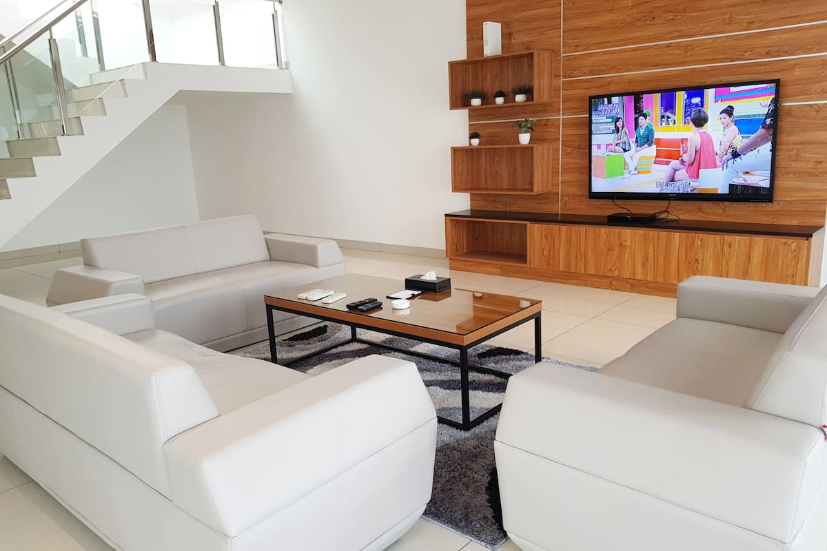 A modern living room with a white sofa set, a coffee table, and a TV mounted on a wooden wall.