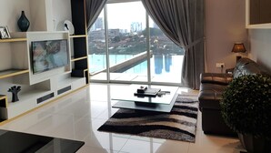 Un salón moderno con un televisor grande, una mesa de centro de cristal, un sofá de cuero y vistas a un paisaje urbano a través de amplias ventanas.