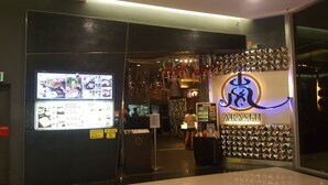 A restaurant entrance with a digital menu display, a sign indicating non-halal options, and a decorative wall with the restaurant's name.
