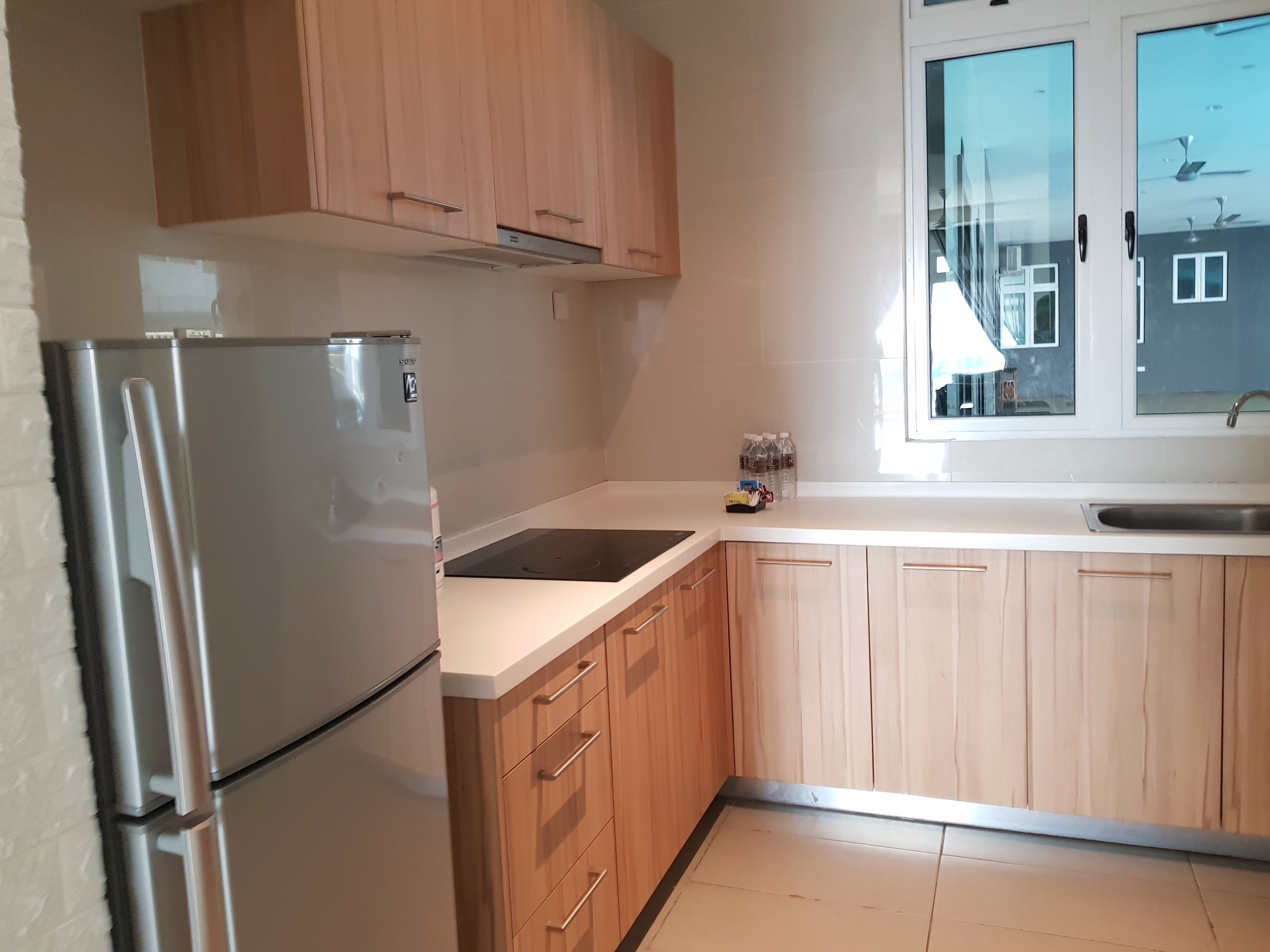 Una cocina con armarios de madera, un refrigerador de acero inoxidable, un lavamanos y un ventanal con vistas a edificios.