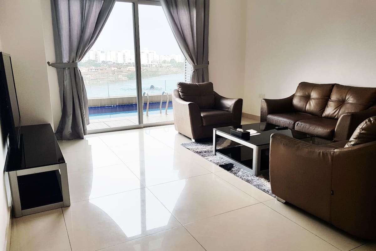 A modern living room with a large window, a flat-screen TV, two leather sofas, and a coffee table.