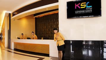 A hotel reception area with a modern design, a reception desk, and a digital sign displaying the hotel name.