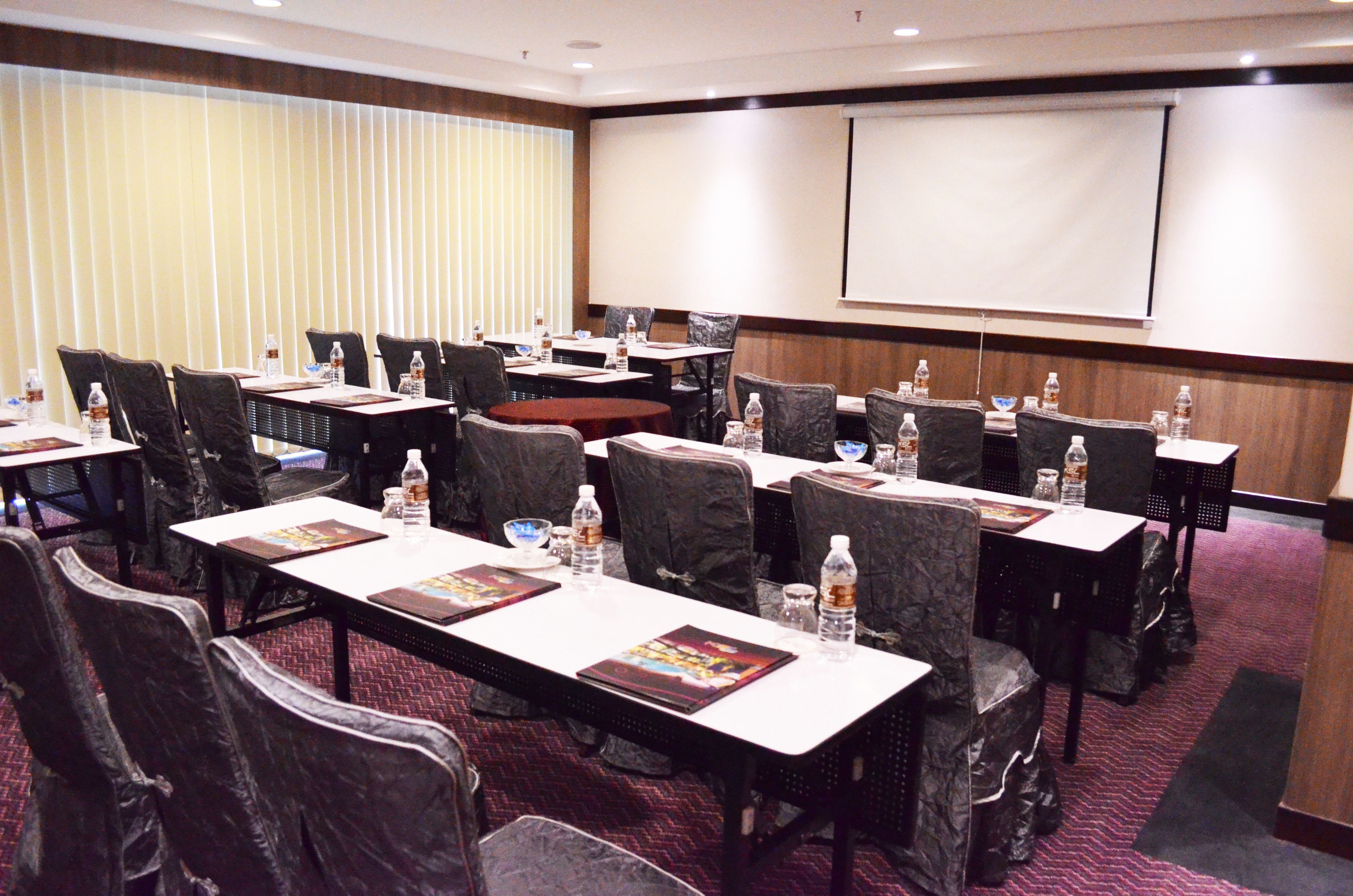 A conference room with multiple tables, chairs, and a large screen.