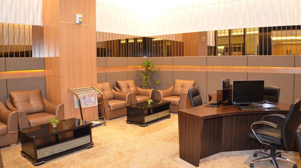 A modern office space with leather sofas, a wooden desk with a computer, and a magazine rack.