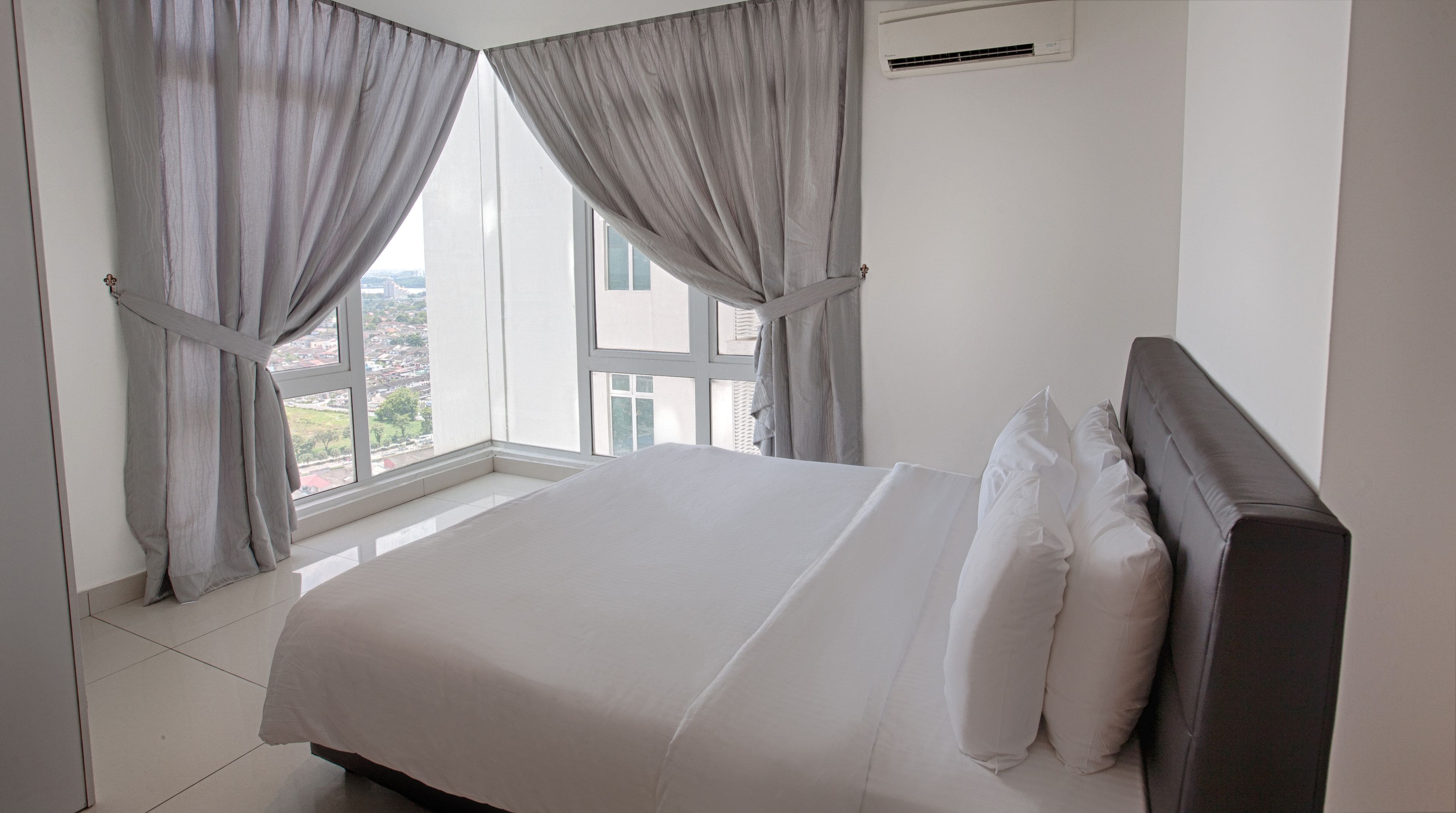 A bedroom with a large bed, grey curtains, and a window with a city view.