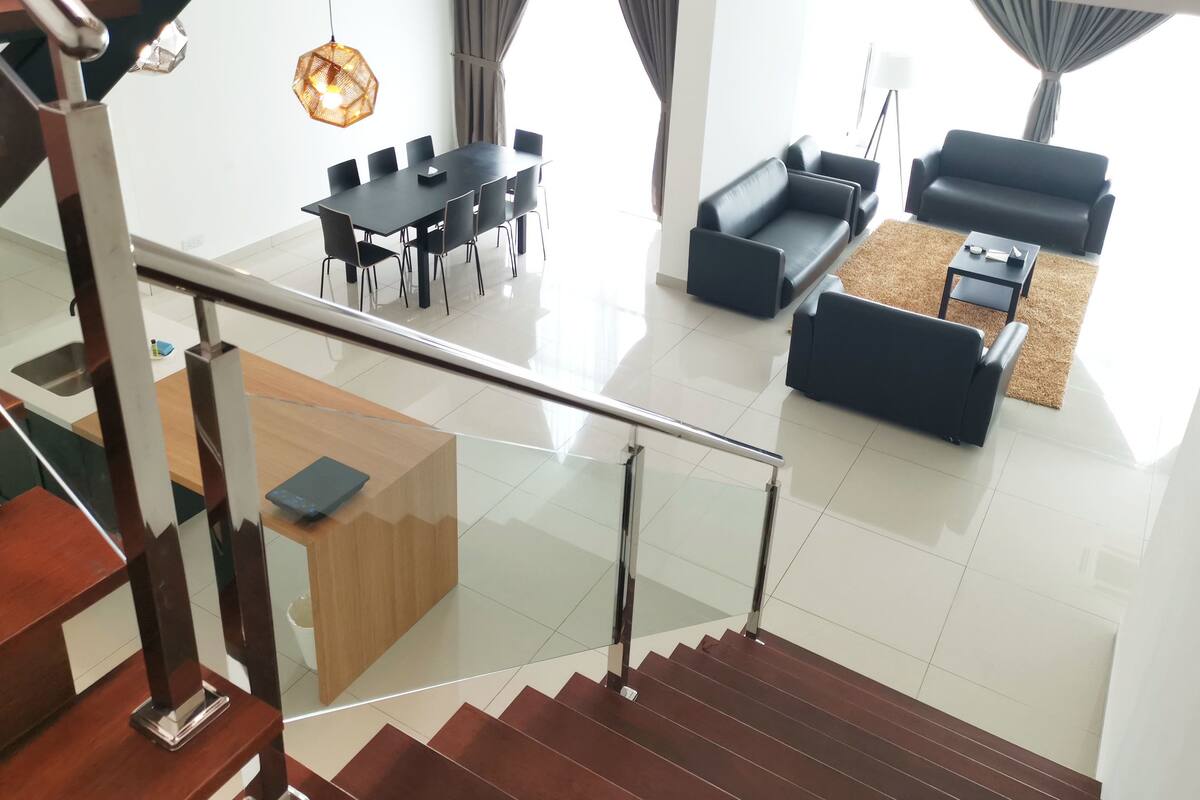 A modern interior with a staircase, a dining area with a black table and chairs, a living room with black sofas, and a large window with curtains.