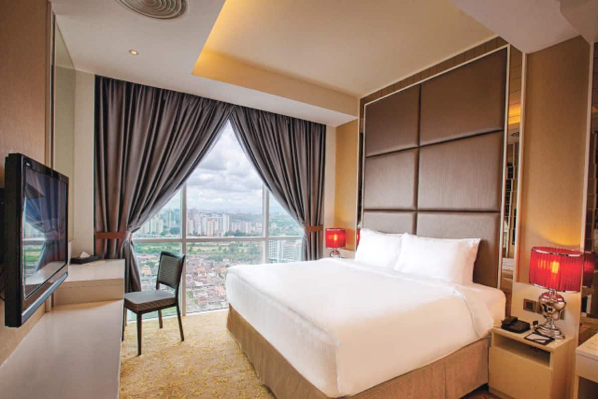 A hotel room with a large bed, a desk with a chair, a TV, and a view of the cityscape.