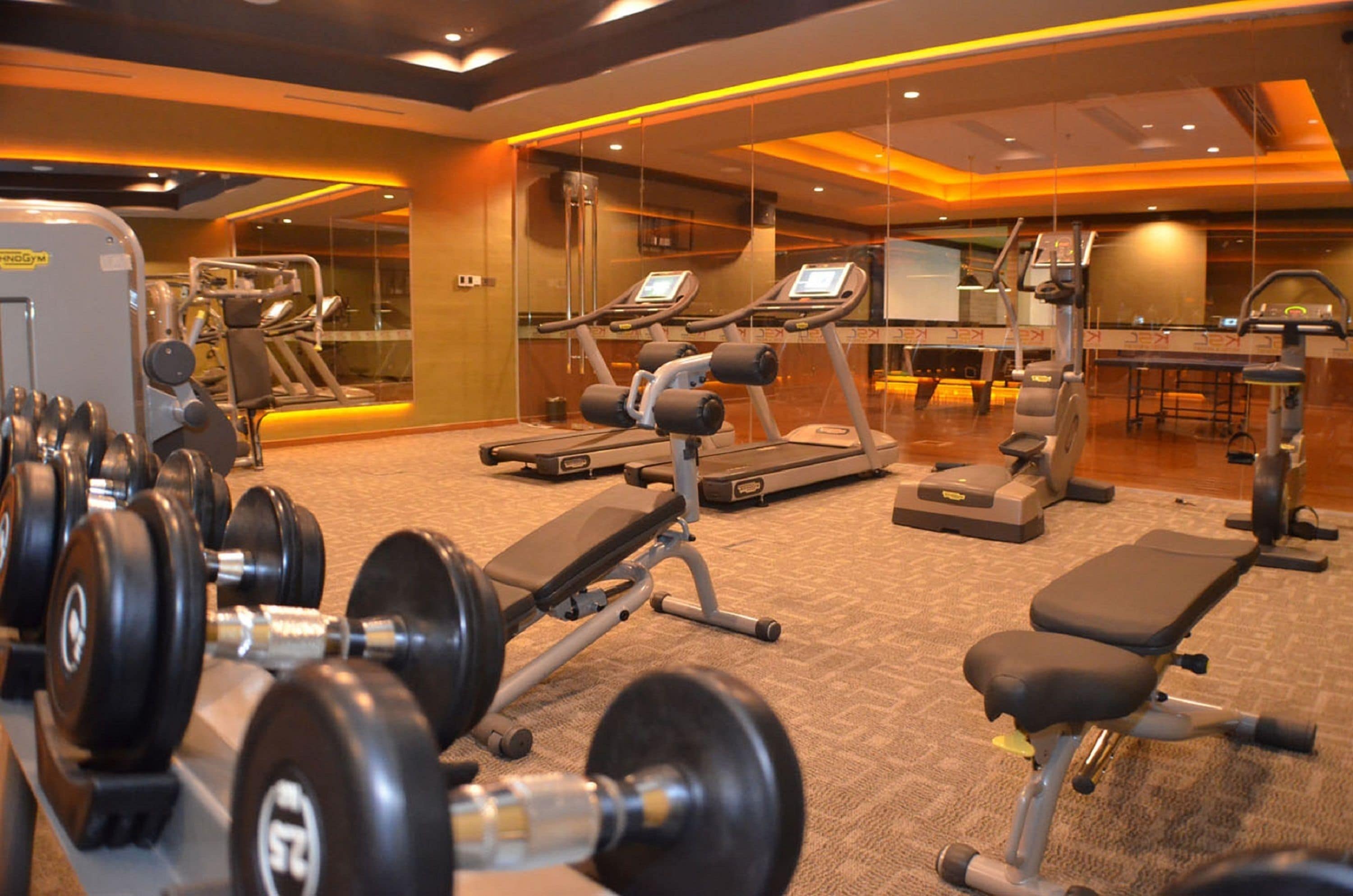 Une salle de sport équipée de divers appareils d’exercice, notamment des tapis de course, des haltères et des appareils de musculation.