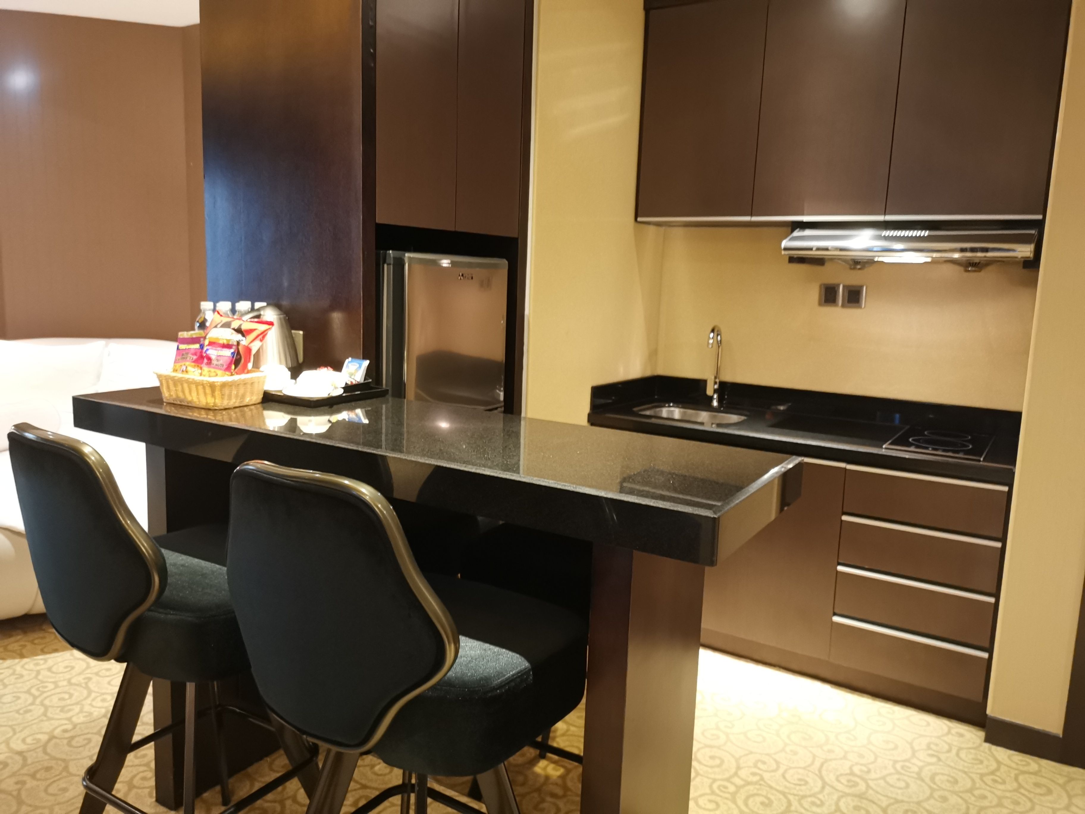 A compact kitchen with a black countertop, two bar stools, a microwave, and a sink.
