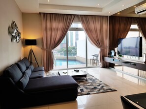 A modern living room with a sofa, a TV, and a pool view.