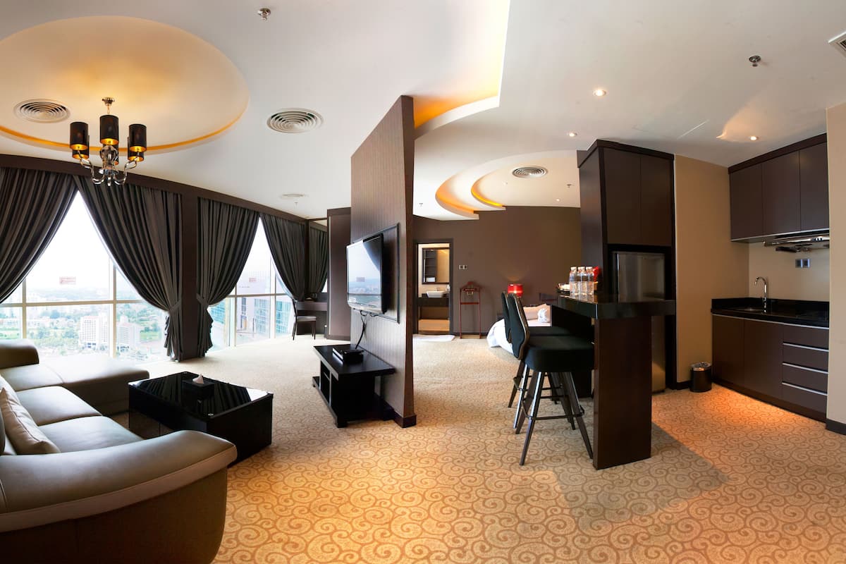 A modern hotel room with a sofa, a TV, a small kitchen area, and a large window offering a city view.