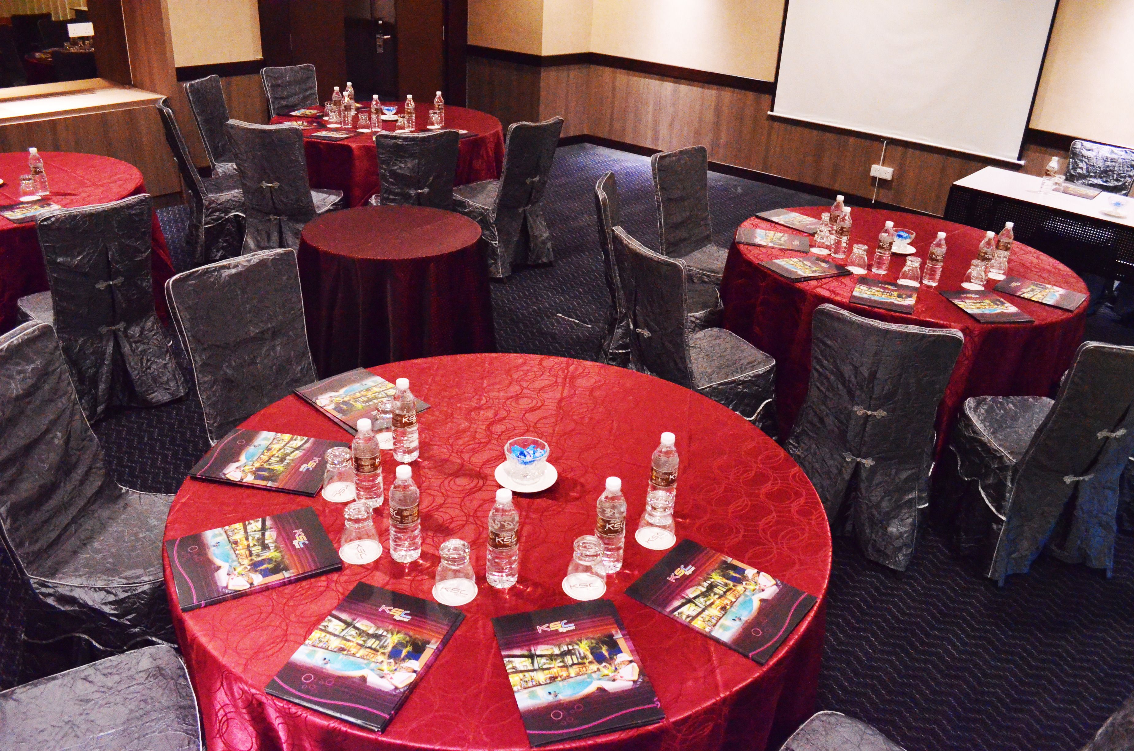 A conference room with round tables covered in red tablecloths, each with brochures, water bottles, and glasses.