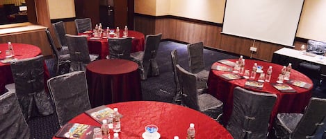 A conference room with round tables covered in red tablecloths, each with brochures, water bottles, and glasses.