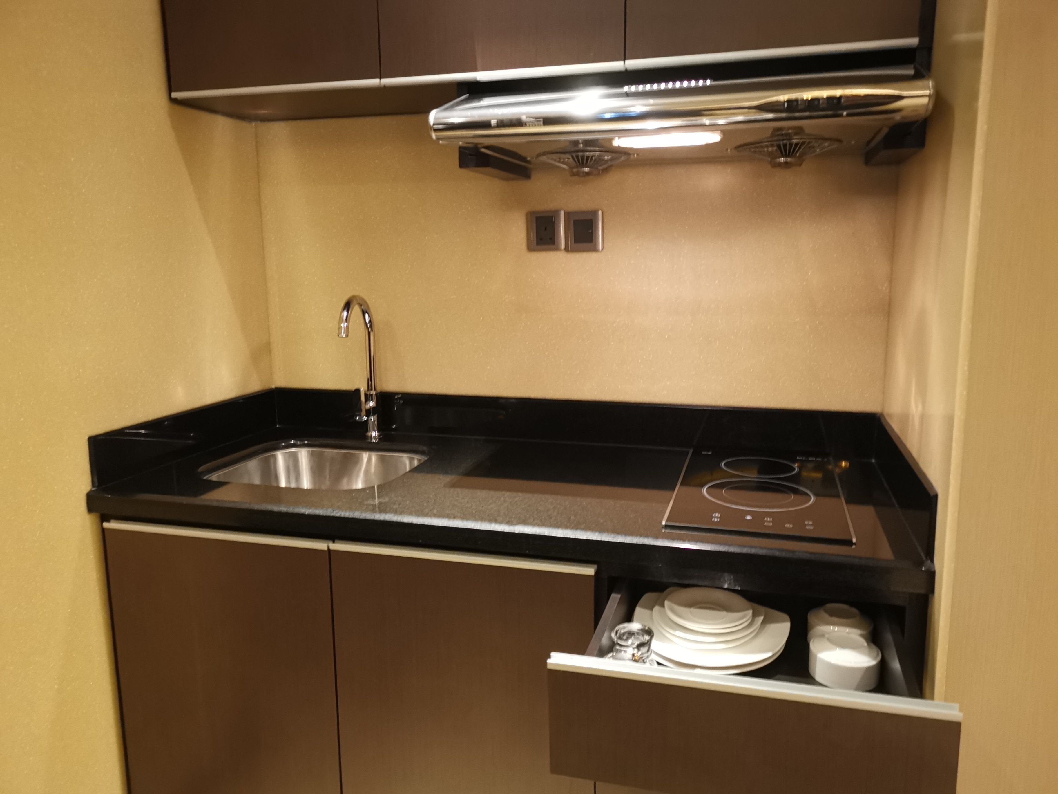 A compact kitchen with a stainless steel sink, a black countertop, and a built-in stove.