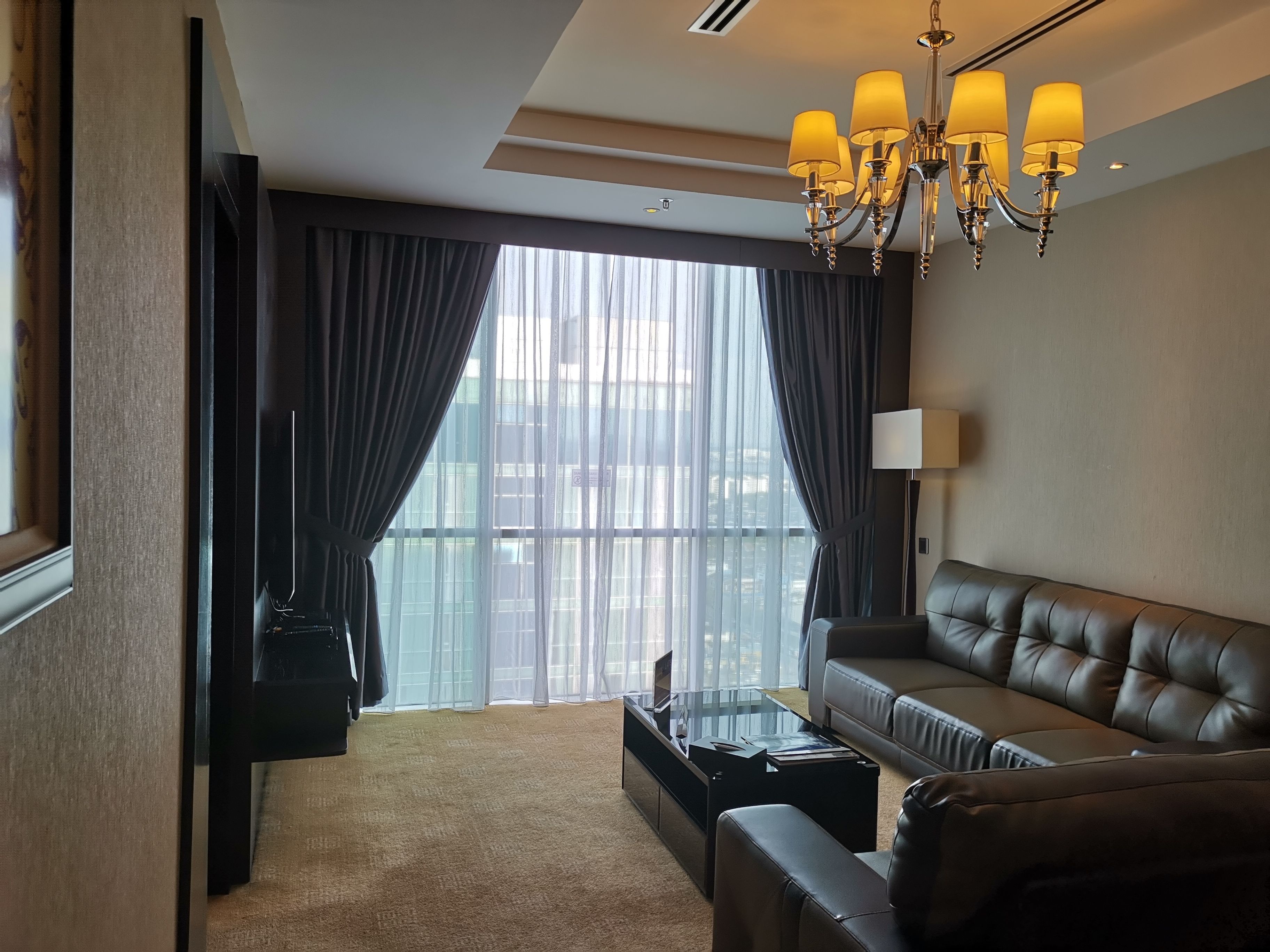 A modern living room with a leather sofa, a glass coffee table, and a chandelier.