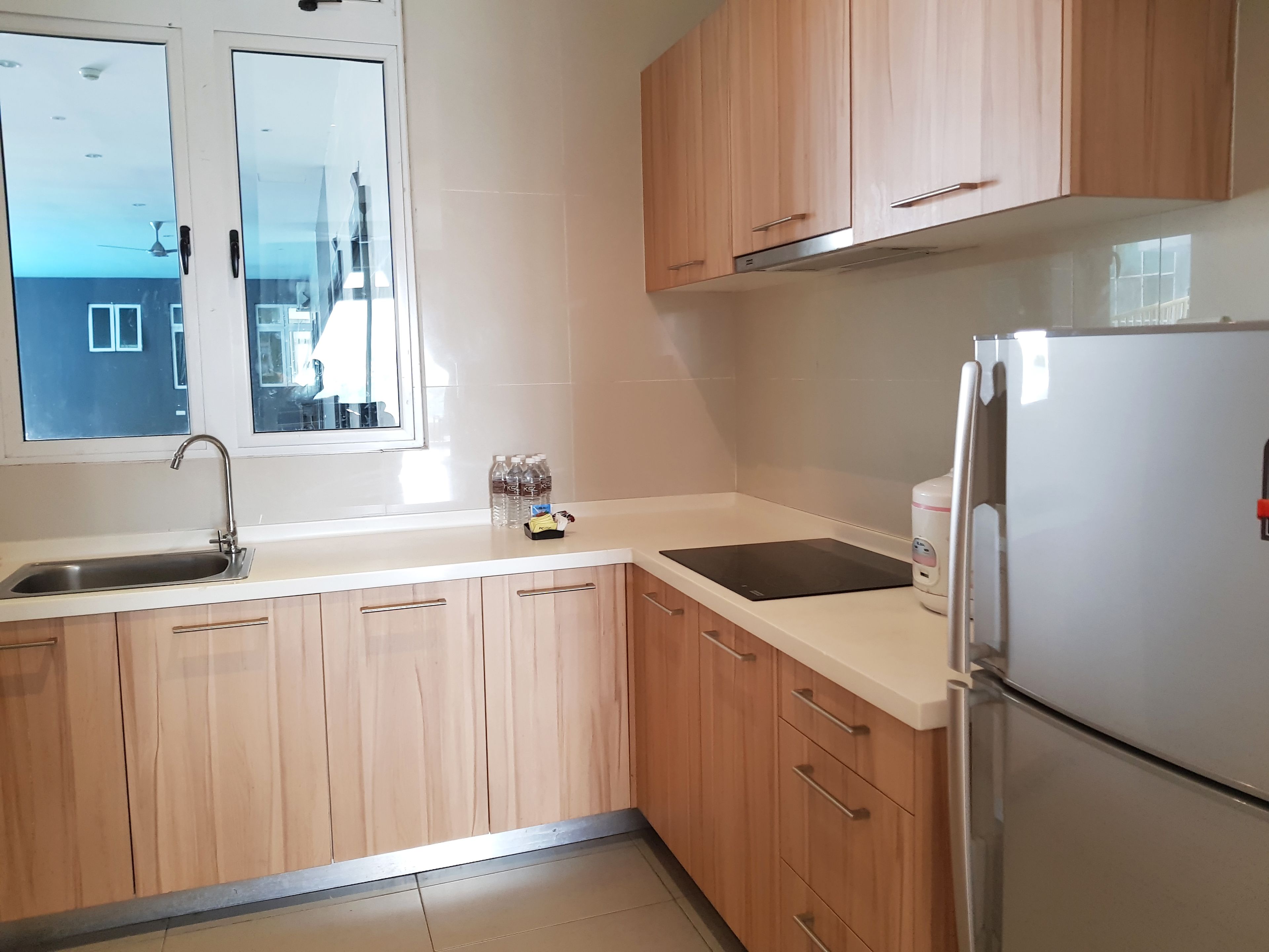 Una cocina con armarios de madera, un lavamanos de acero inoxidable, una ventana y un refrigerador blanco.