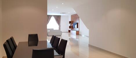 Una sala de estar moderna con comedor, que incluye una mesa grande y sillas, un sofá y un mueble empotrado para entretenimiento.