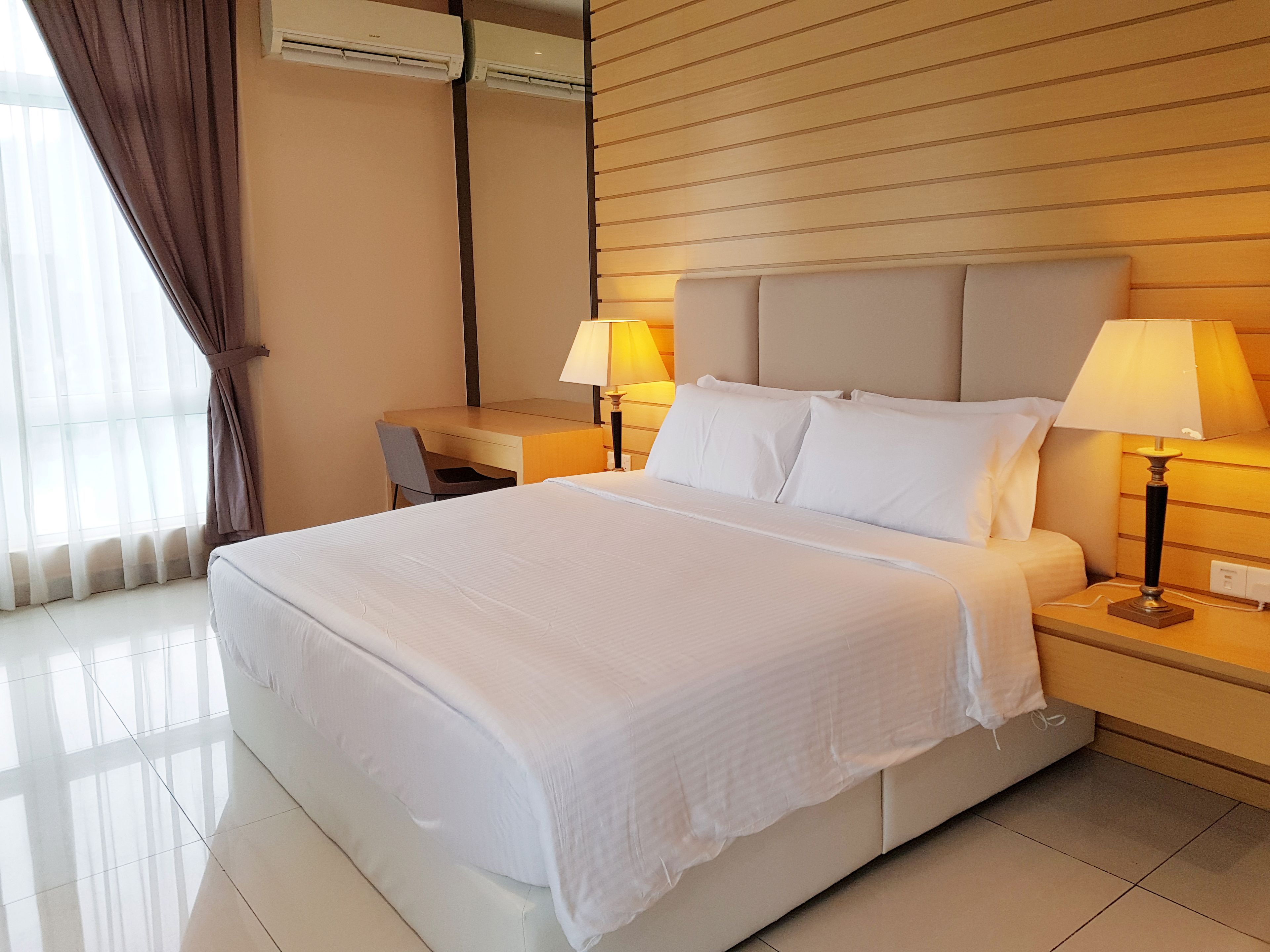 Una habitación de hotel con una cama, dos mesitas de noche con lámparas, un escritorio y un aire acondicionado.