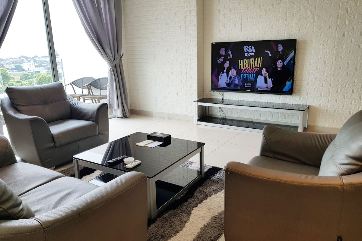 A modern living room with grey sofas, a glass coffee table, and a flat-screen TV mounted on a textured wall.