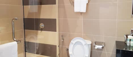 Un baño con cabina de ducha de vidrio, inodoro y toallero con toallas.