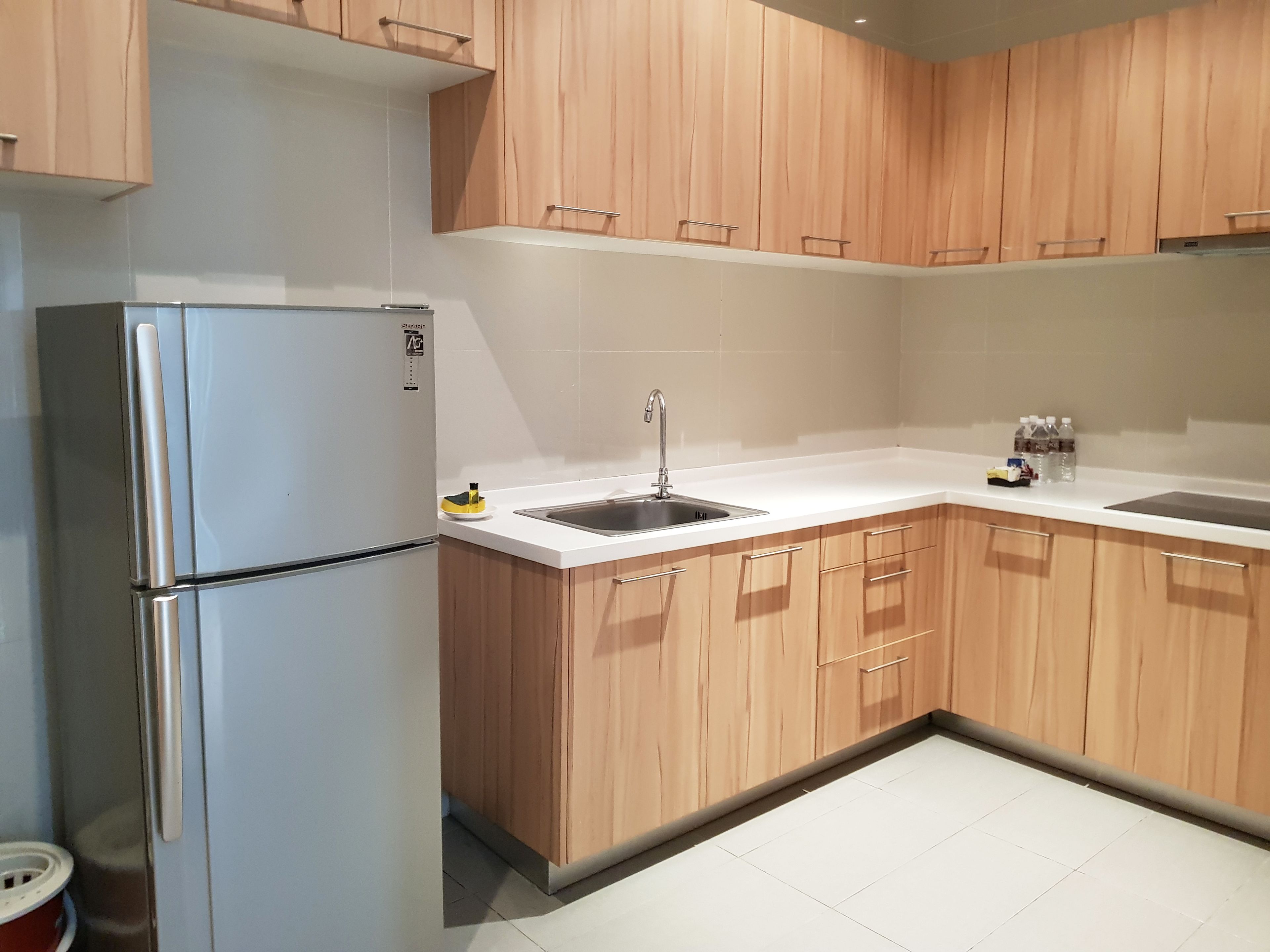 A kitchen with wooden cabinets, a stainless steel refrigerator, a sink, and a white countertop.