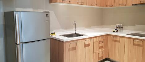 A kitchen with wooden cabinets, a stainless steel refrigerator, a sink, and a white countertop.