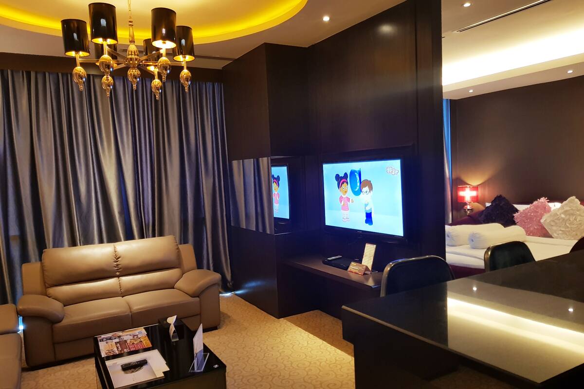 A modern hotel room with a leather sofa, a flat-screen TV, a desk, and a chandelier.