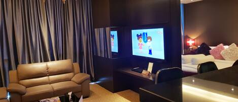 A modern hotel room with a leather sofa, a flat-screen TV, a desk, and a chandelier.