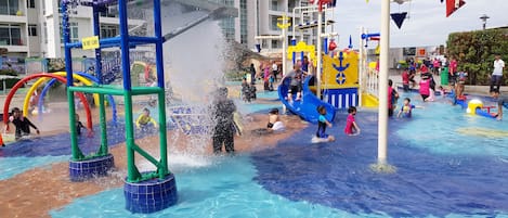 Zona de juegos acuáticos con toboganes y chorros de agua, rodeada por una piscina.