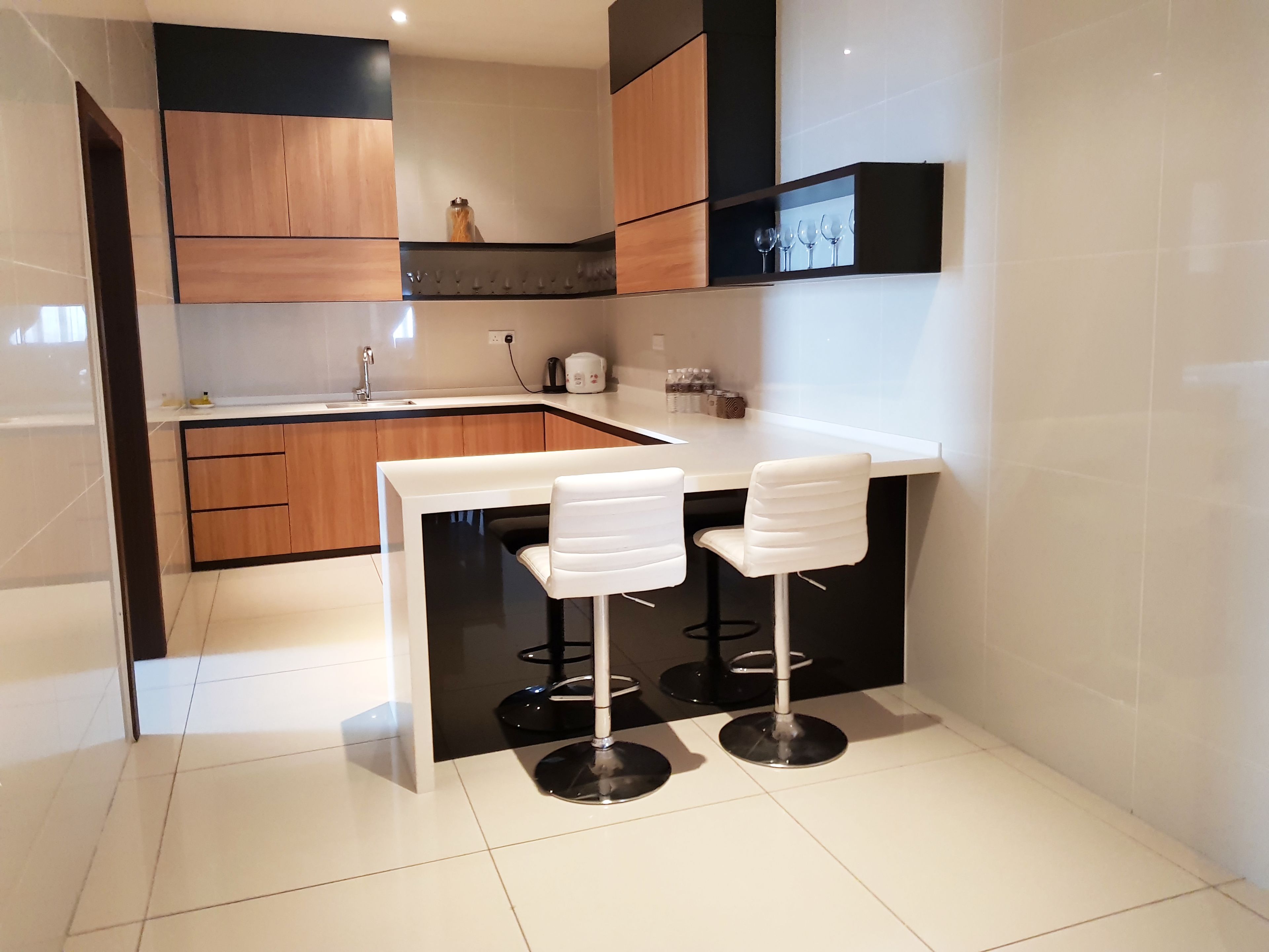 A modern kitchen with wooden cabinets, a white countertop, and two white bar stools.