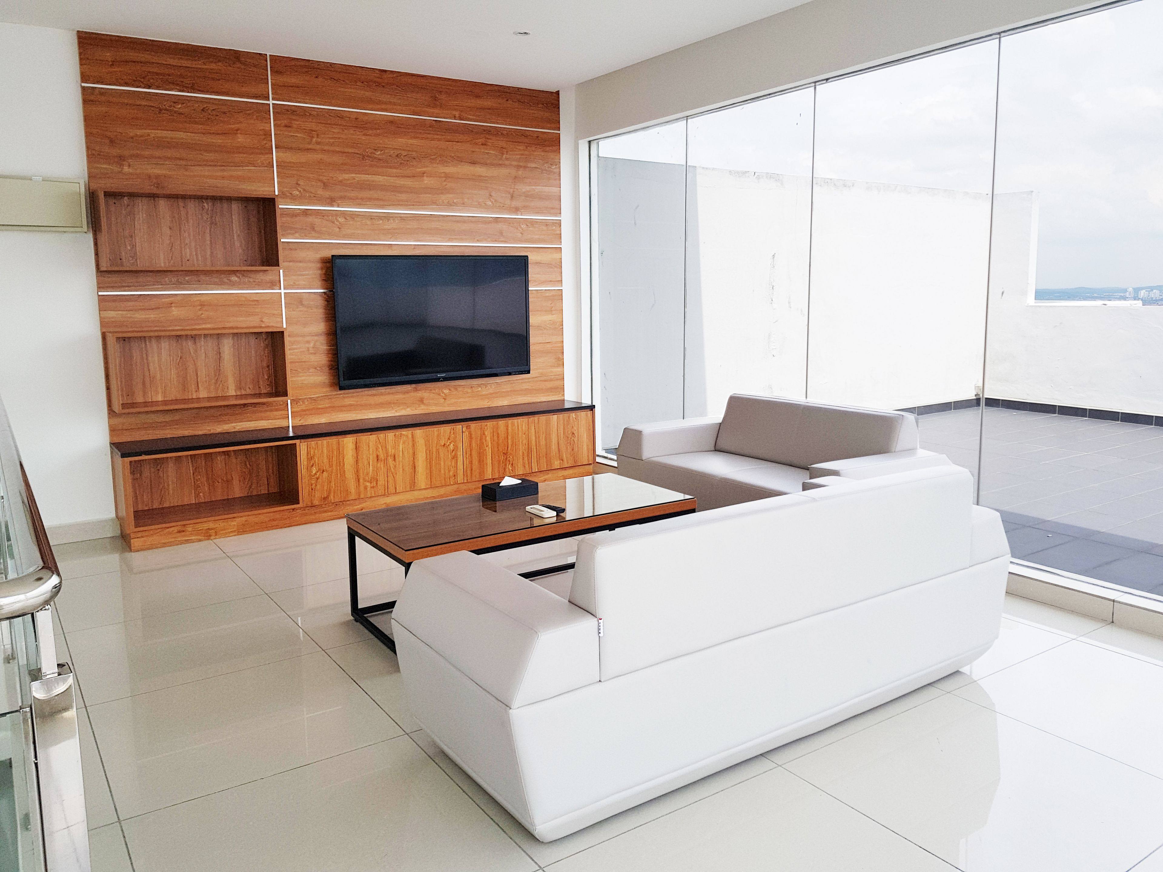 A modern living room with a flat-screen TV mounted on a wooden wall, a white sofa, and a glass coffee table.