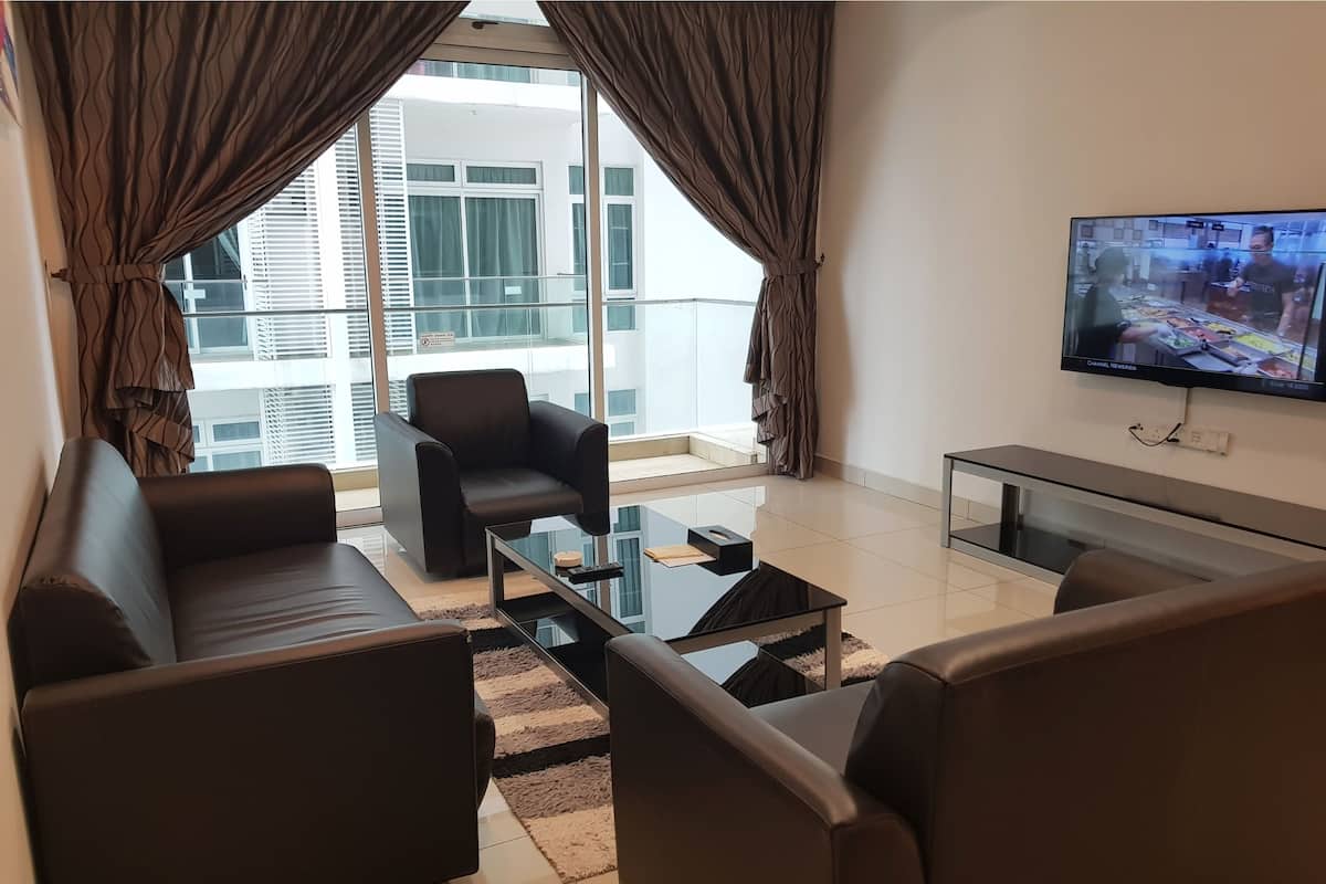 A modern living room with a sofa, armchair, and a glass coffee table. A flat-screen TV is mounted on the wall.