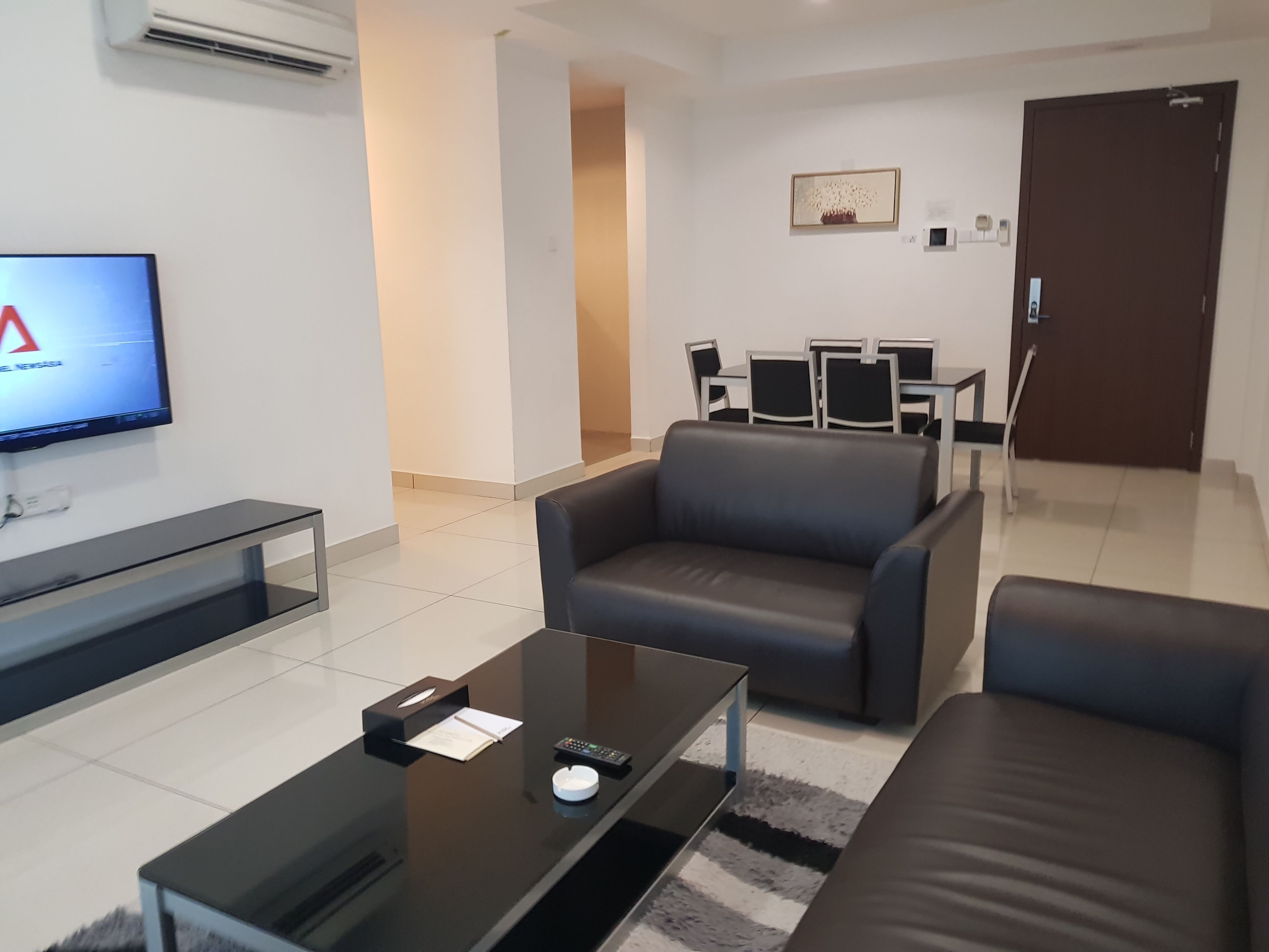 Ein modernes Wohnzimmer mit Flachbildfernseher, Glastisch und schwarzem Ledersofa.