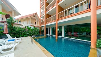 Un área de piscina con sillones de descanso y un edificio de varios pisos con balcones.