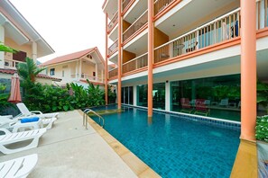 A swimming pool area with lounge chairs and a multi-story building with balconies. - Aonang Regent (Krabi)