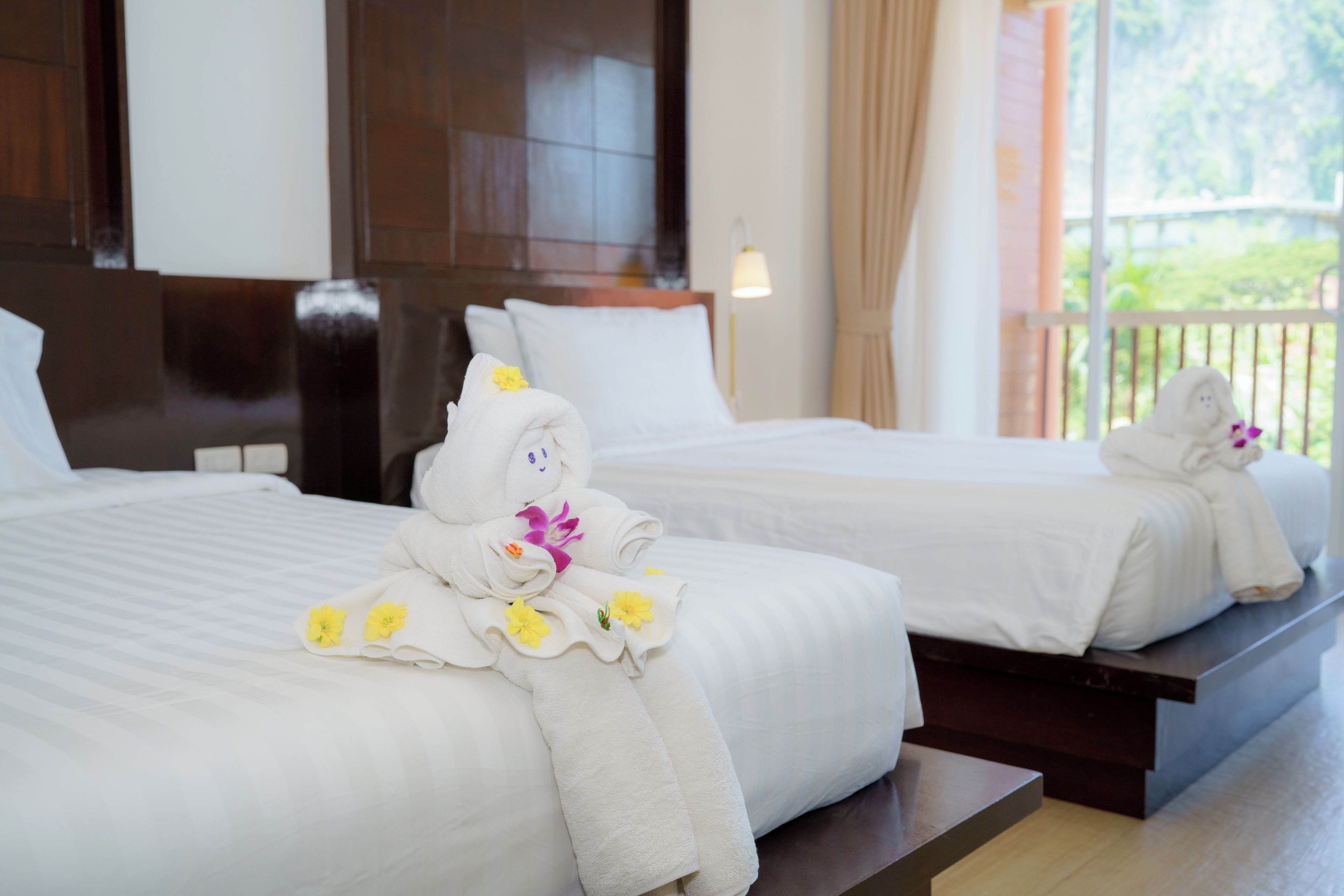 Quarto de hotel com duas camas, cada uma com uma toalha dobrada e uma flor.
