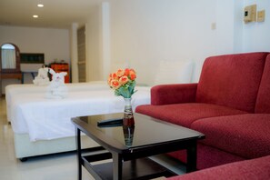 A hotel room with a bed, a red sofa, a small table with a vase of flowers, and a remote control on the table. - Aonang Regent (Krabi)