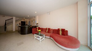 Una sala de estar con un sofá rojo curvo, una pequeña mesa blanca y un mostrador de recepción.