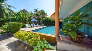 Una piscina con sillas de descanso, rodeada de plantas tropicales y un cielo despejado.