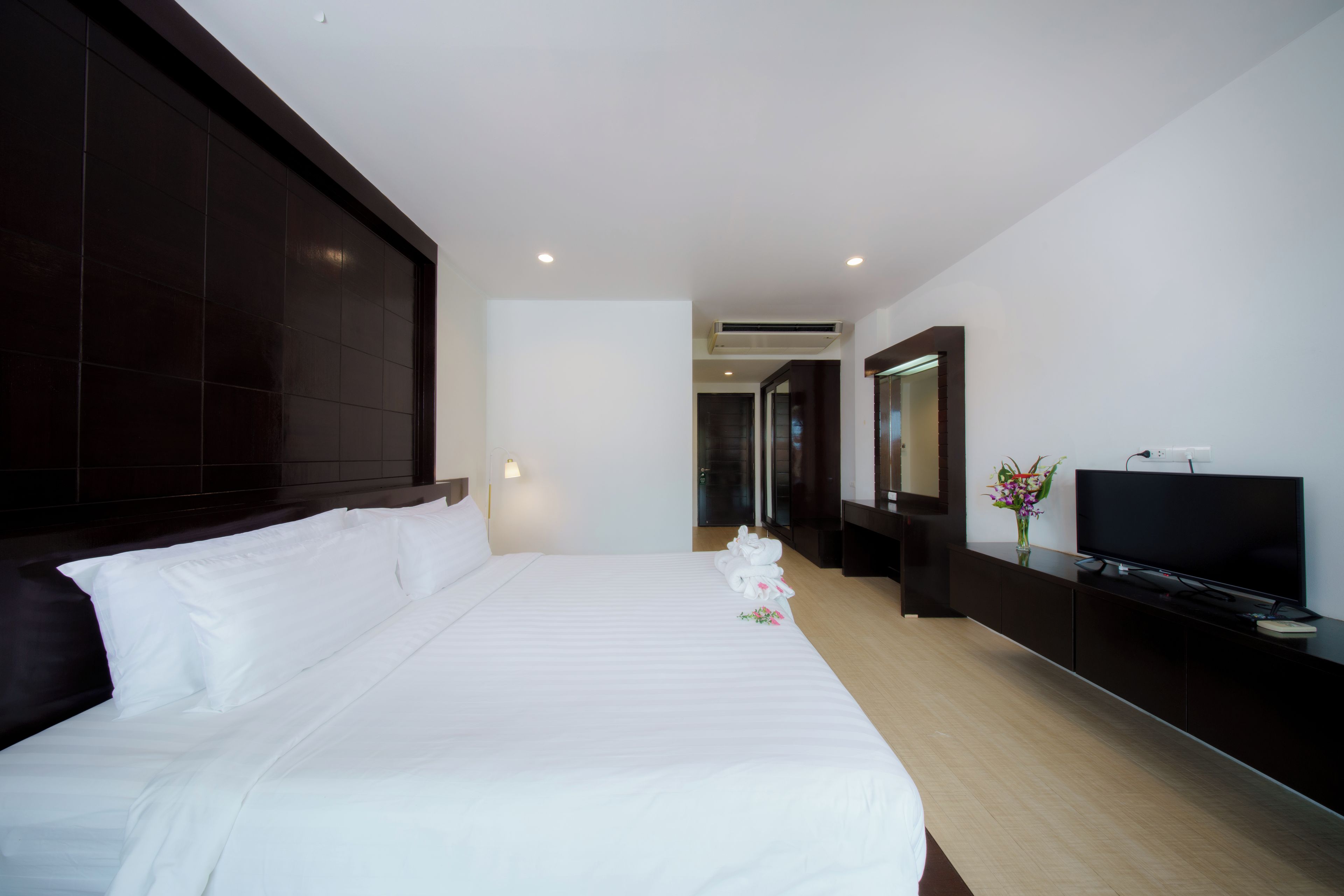 Une chambre d’hôtel avec un grand lit, un téléviseur à écran plat, une commode en bois foncé et un miroir au mur.