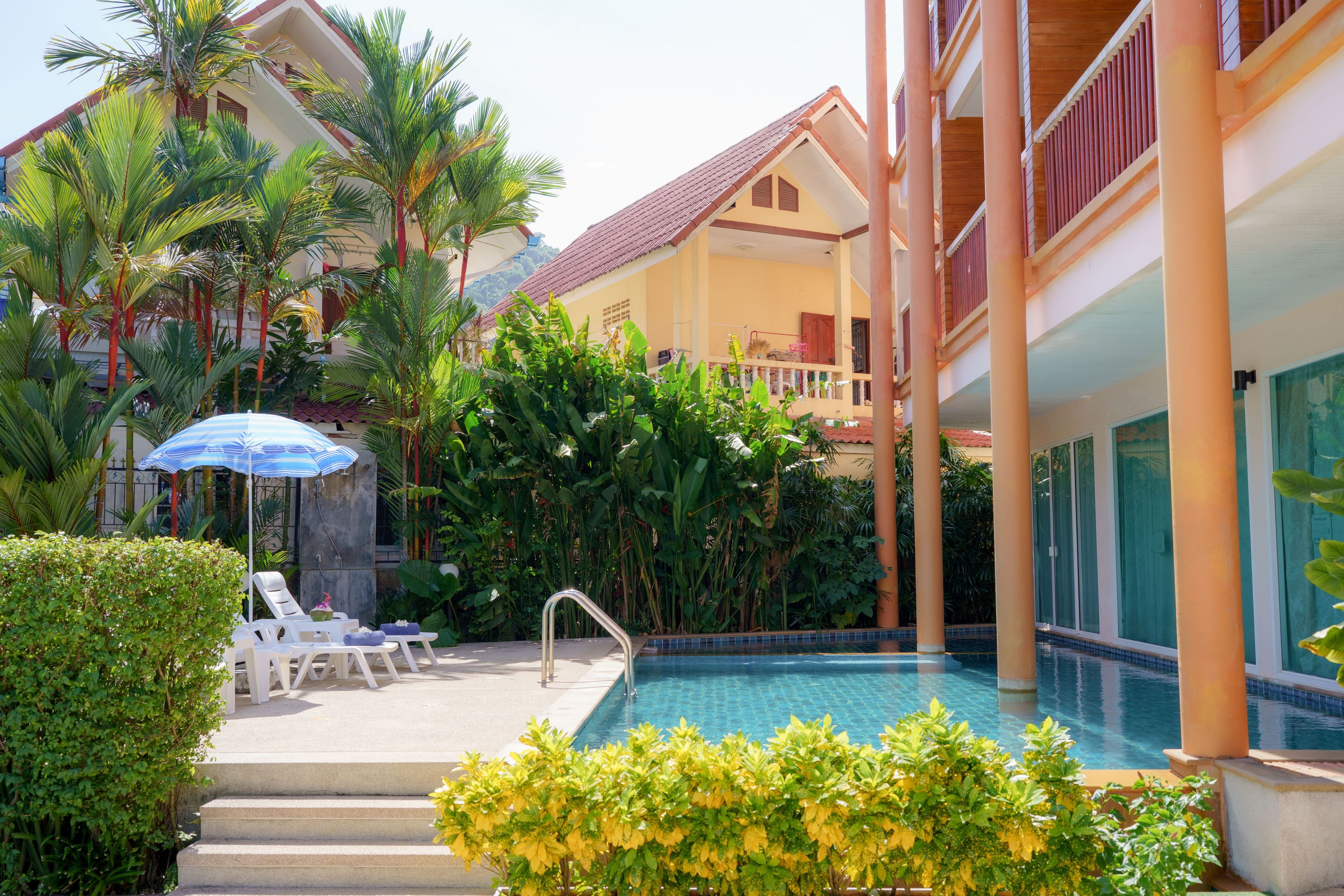 A pool area with lounge chairs, a blue umbrella, and lush greenery.