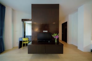 Una sala moderna con un televisor de pantalla plana sobre un mueble de madera oscura, un sillón amarillo y un jarrón con flores.